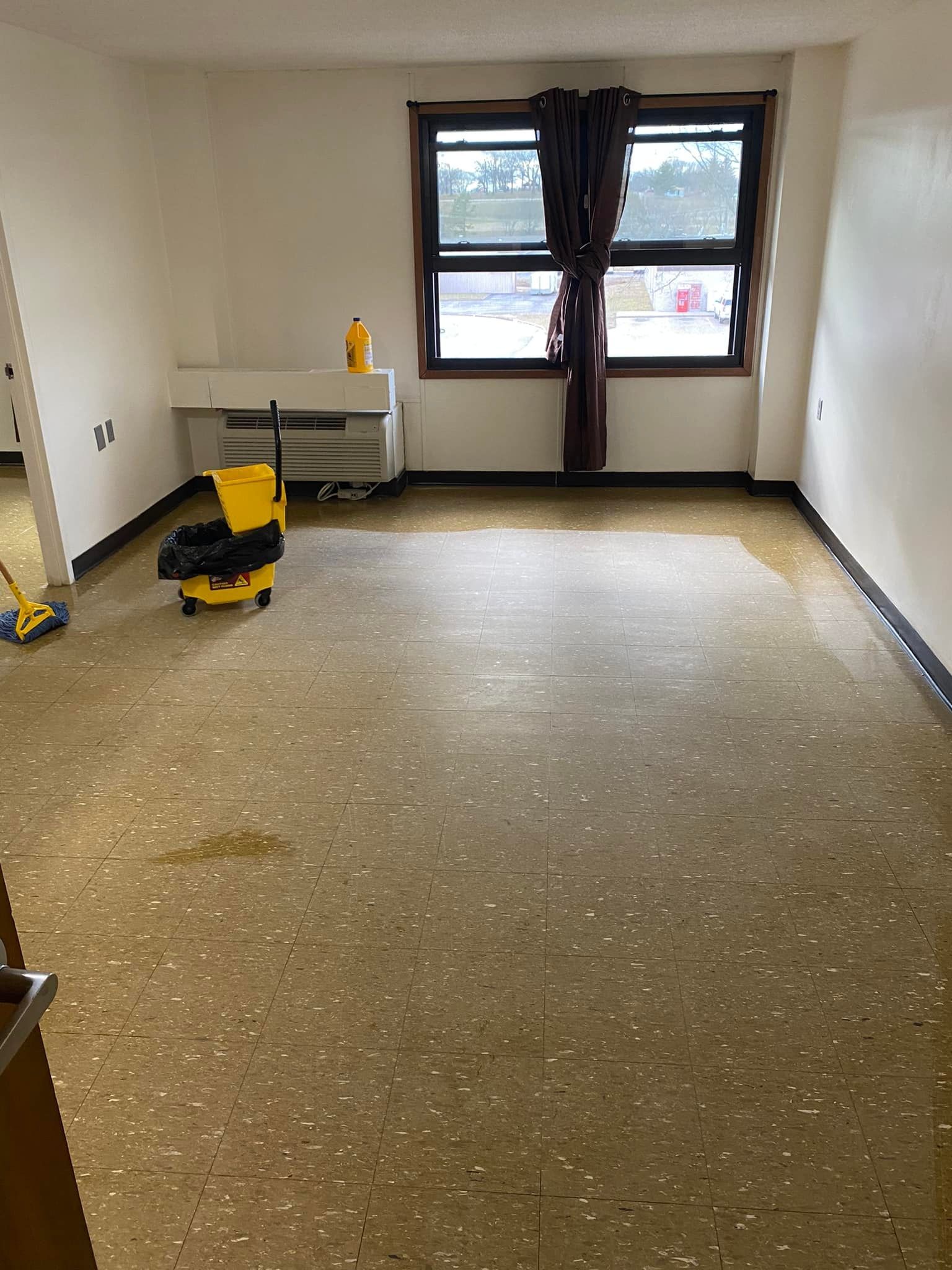 An empty room with a yellow mop and bucket on the floor.
