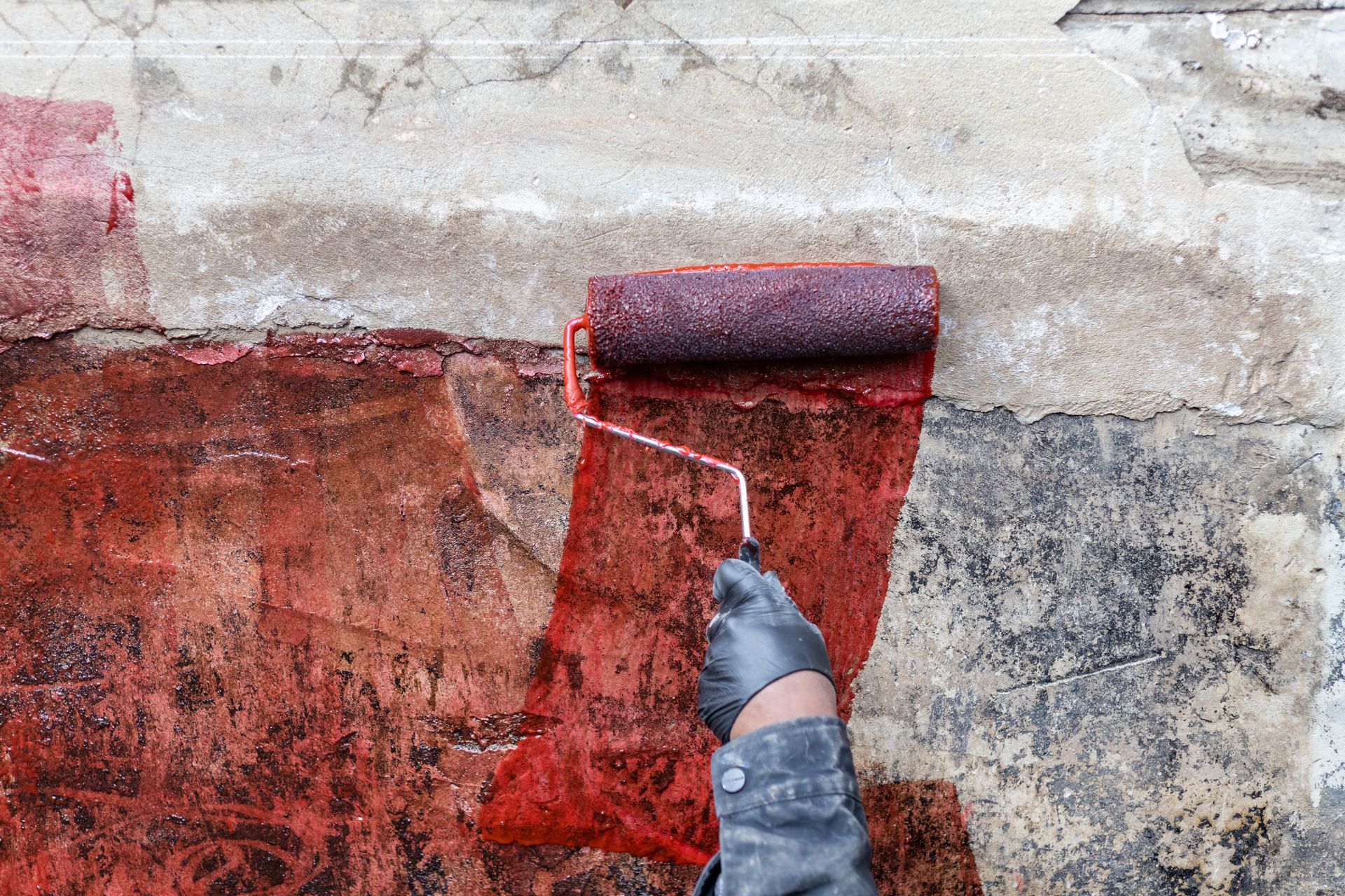 A man wearing a mask and yellow gloves is working on a wall