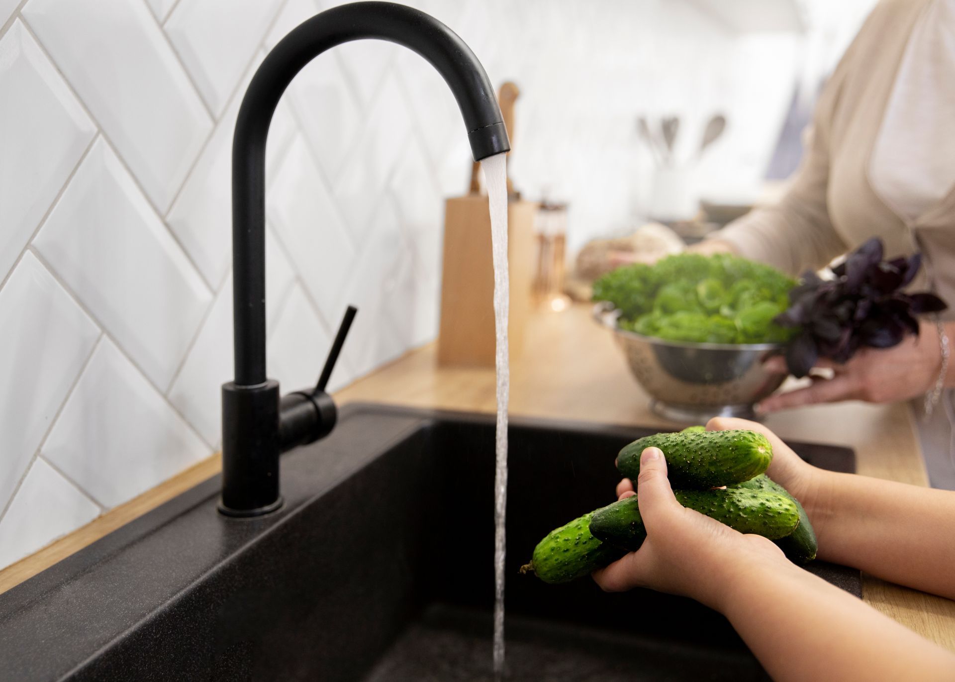 A person is washing cucumbers in a kitchen sink.