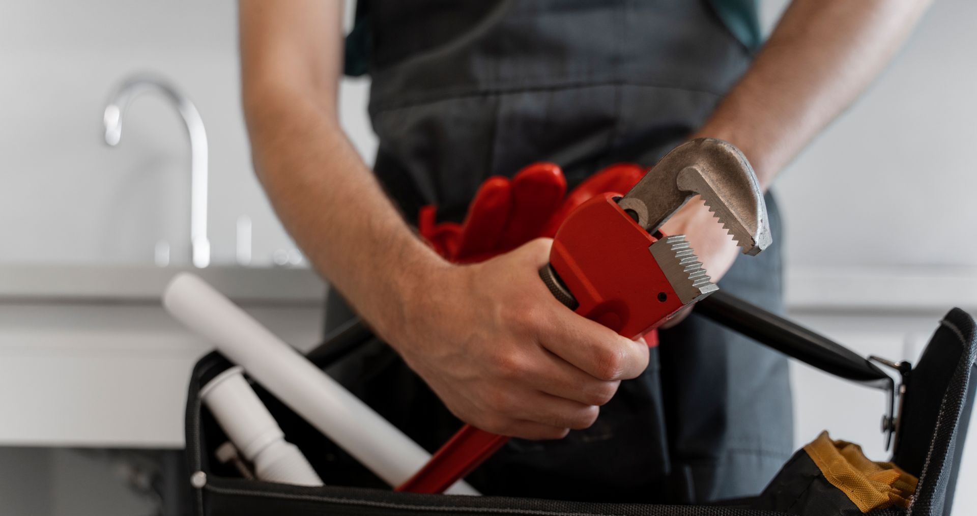 A plumber is holding a wrench in front of a toolbox.