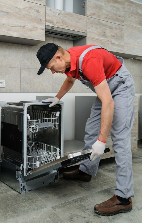 A man is fixing a dishwasher in a kitchen.