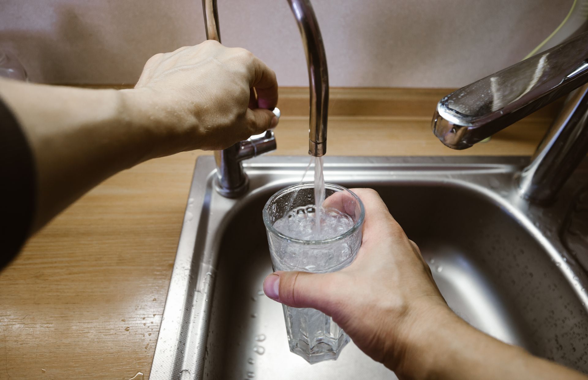 A person is pouring water into a glass in a sink.