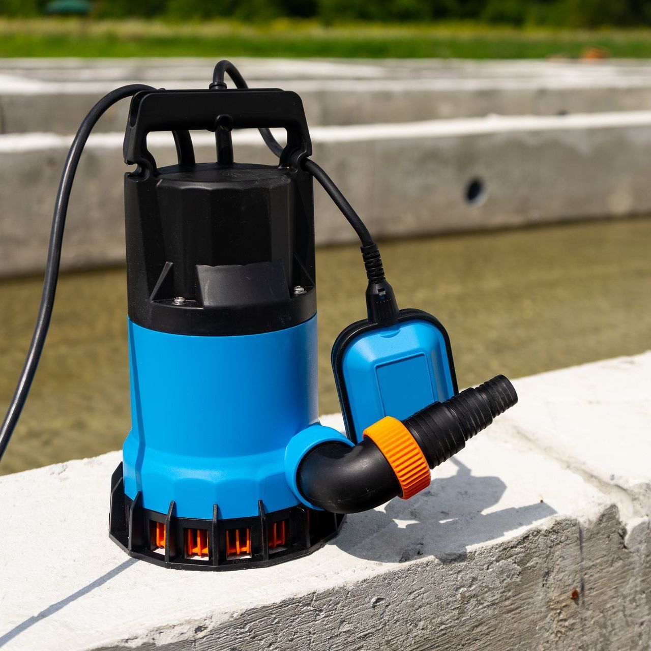 A blue and black water pump is sitting on a concrete wall.