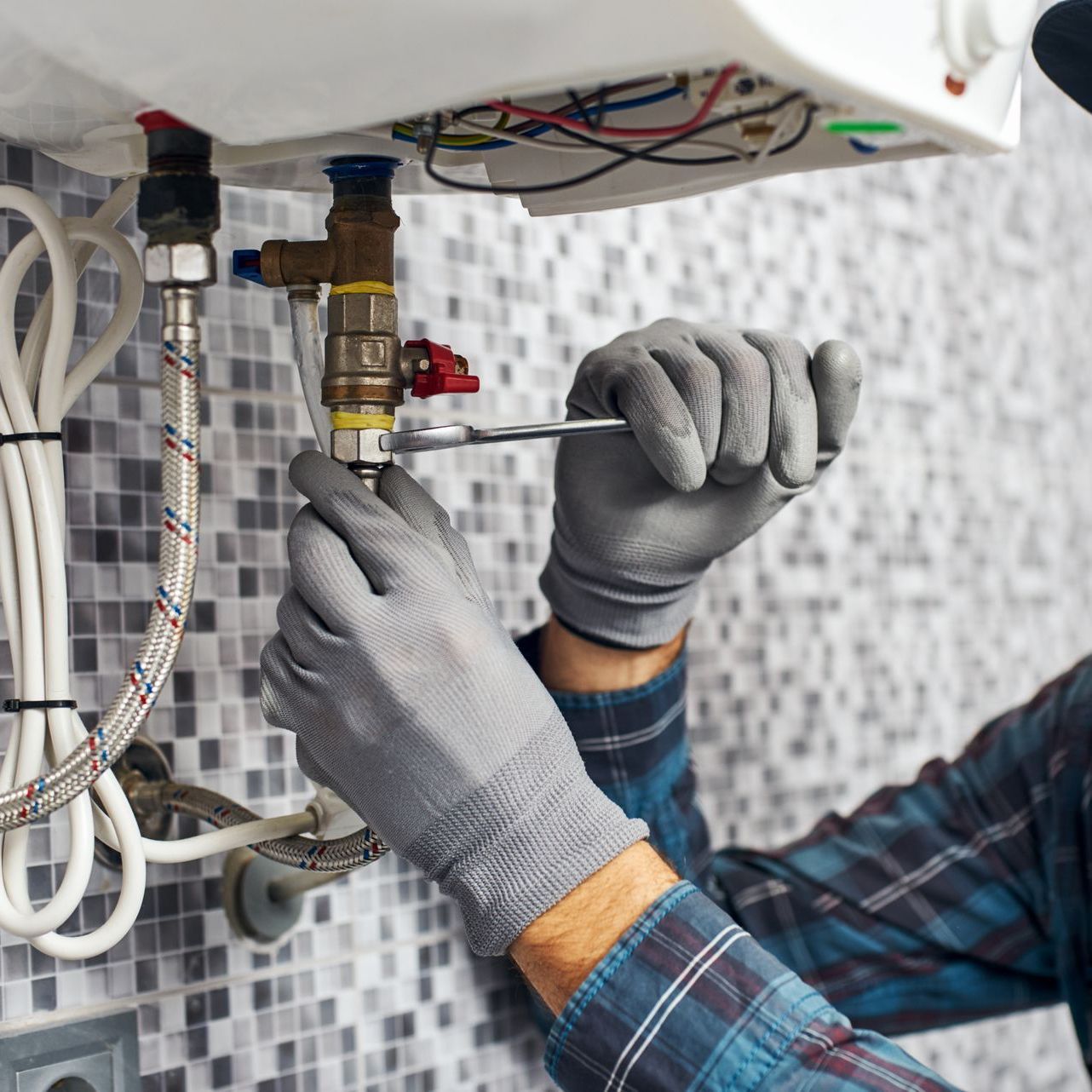 A man is fixing a water heater with a wrench.