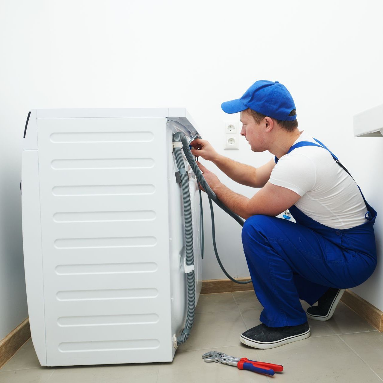 A man in blue overalls is working on a washing machine.