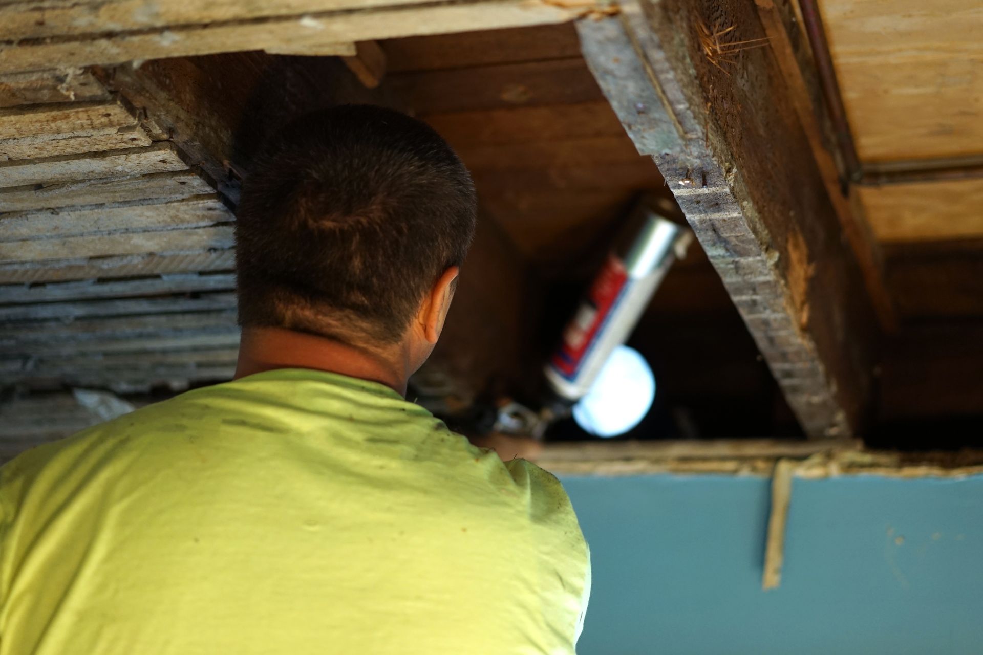 A man in a green shirt is working under a wooden ceiling.