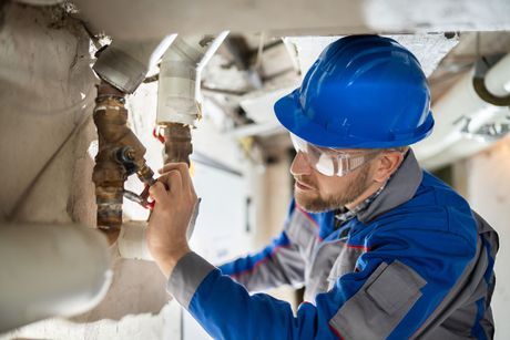 A man wearing a hard hat and safety glasses is working on a pipe.