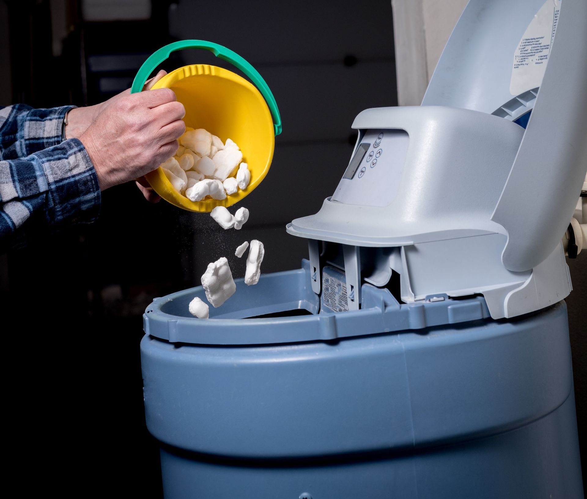 A person is pouring a yellow bucket of soap into a water softener