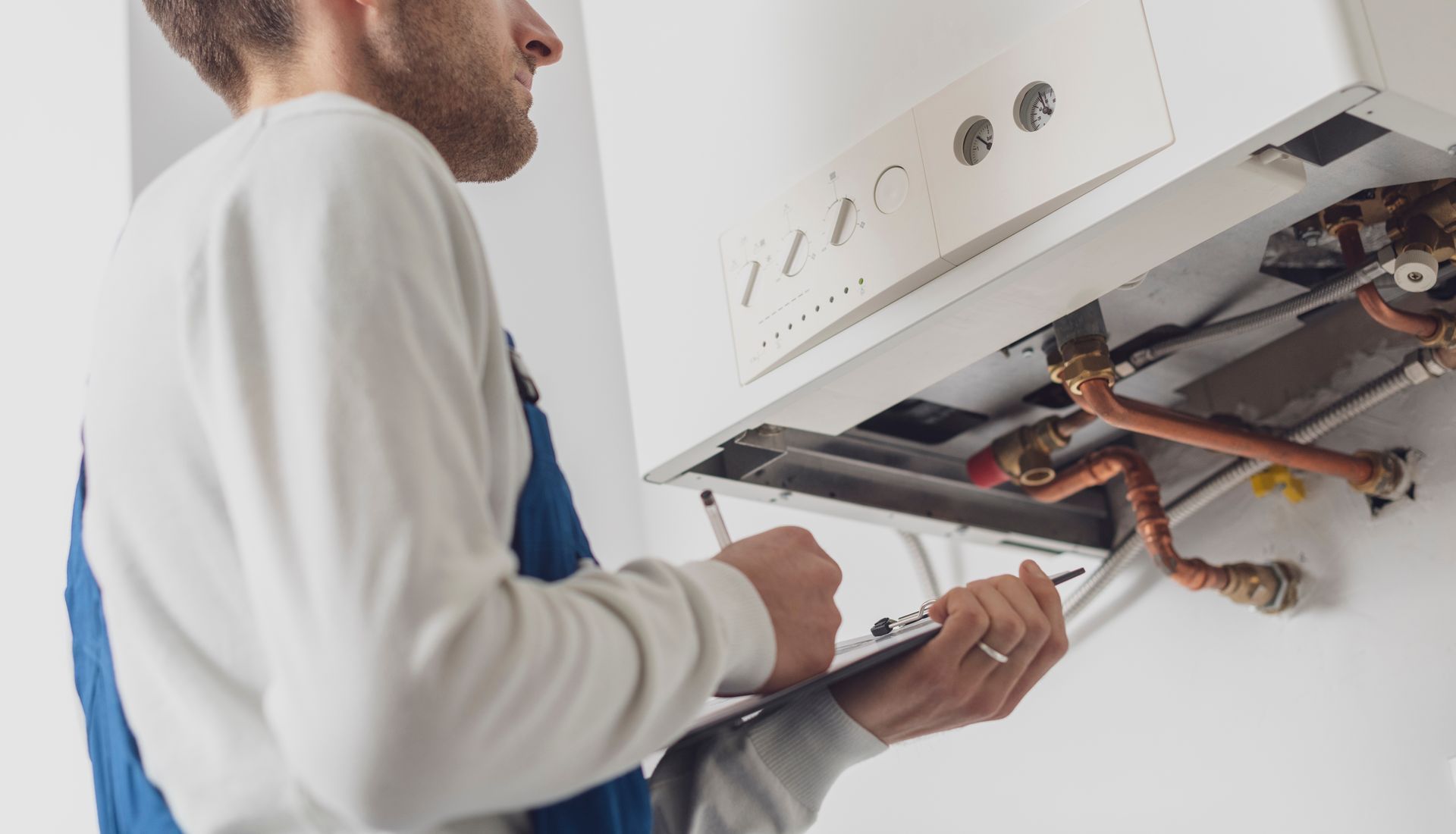 A man is fixing a boiler with a wrench and a clipboard.