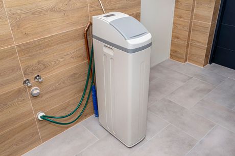 A water softener is sitting in a bathroom next to a hose.