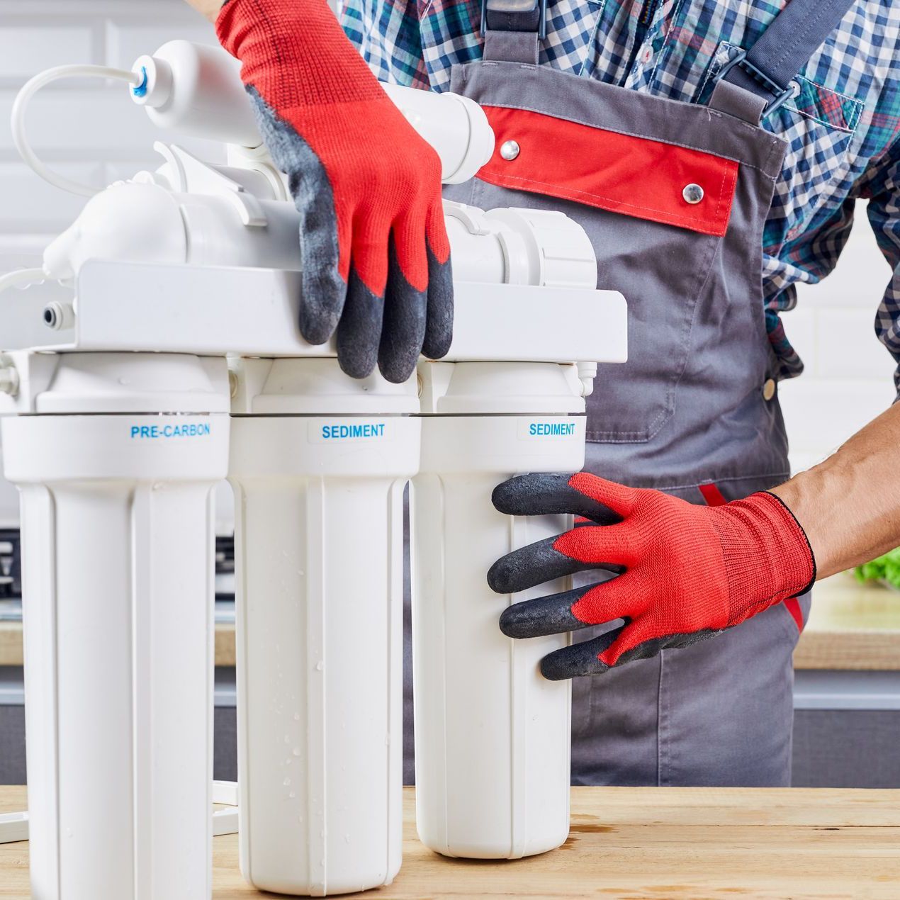 A man wearing red gloves is working on a water filter.