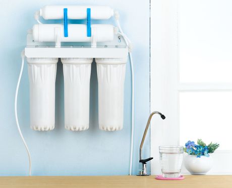 A water filter is hanging on a wall next to a glass of water.