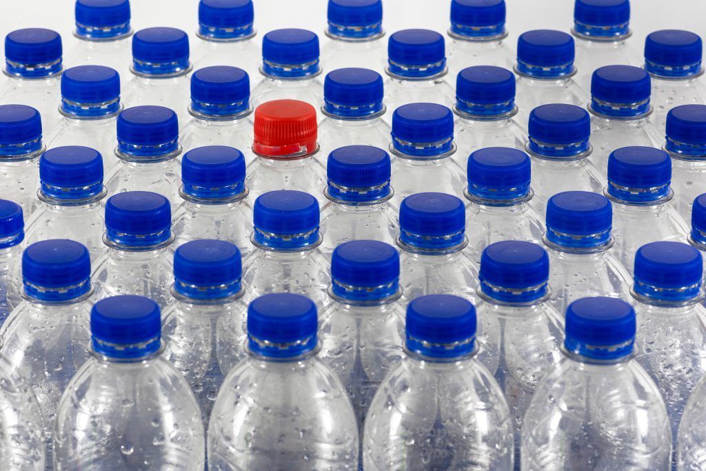 A row of plastic water bottles with blue caps and a red cap in the middle.