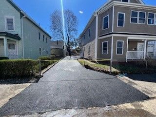 Paved driveway between two-story houses; bright sunlight casts a shadow.