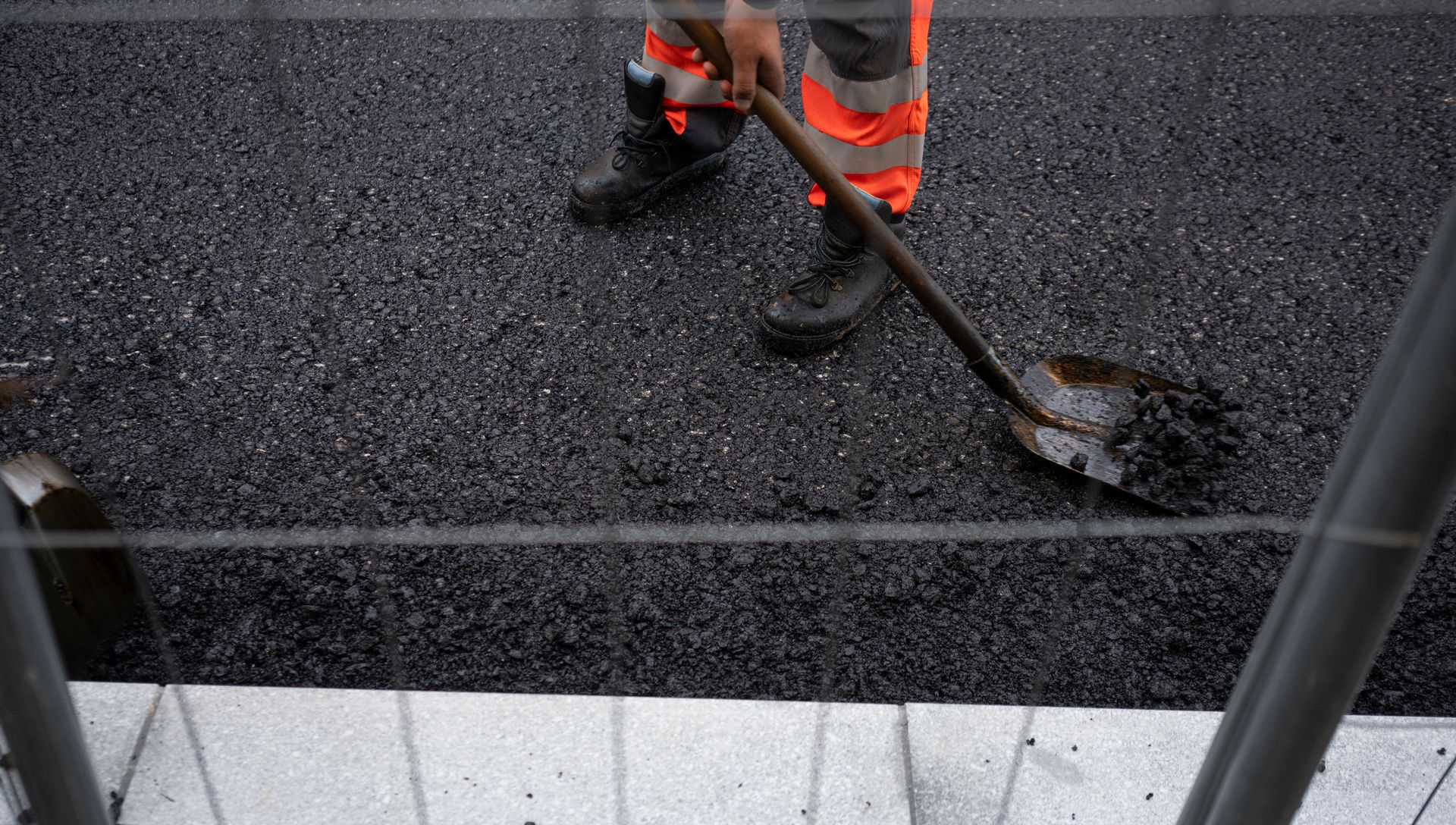 A man uses a shovel to spread asphalt, showcasing the work of a parking lot paving contractor.