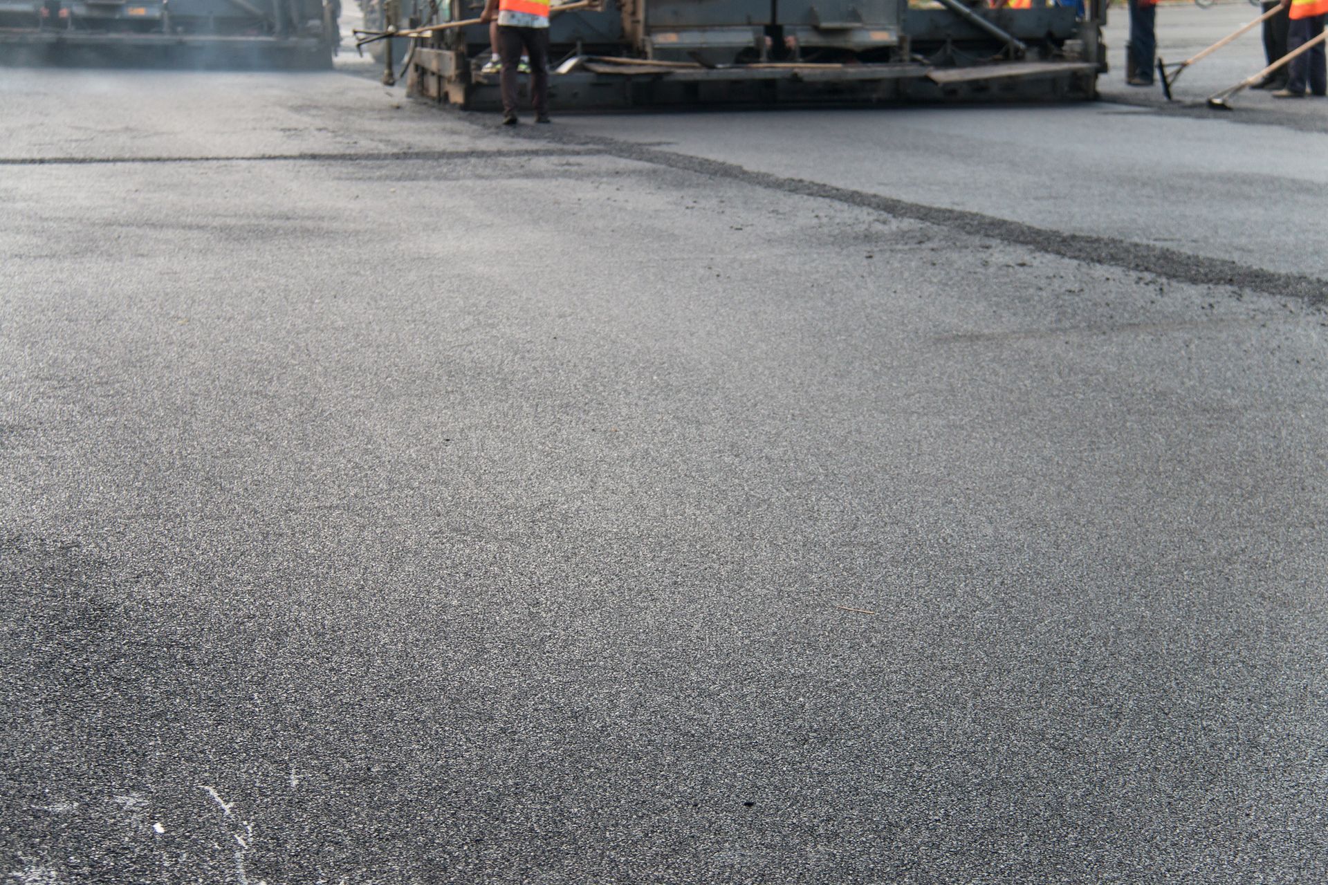 Fresh asphalt paving on road with construction workers and machinery during resurfacing.