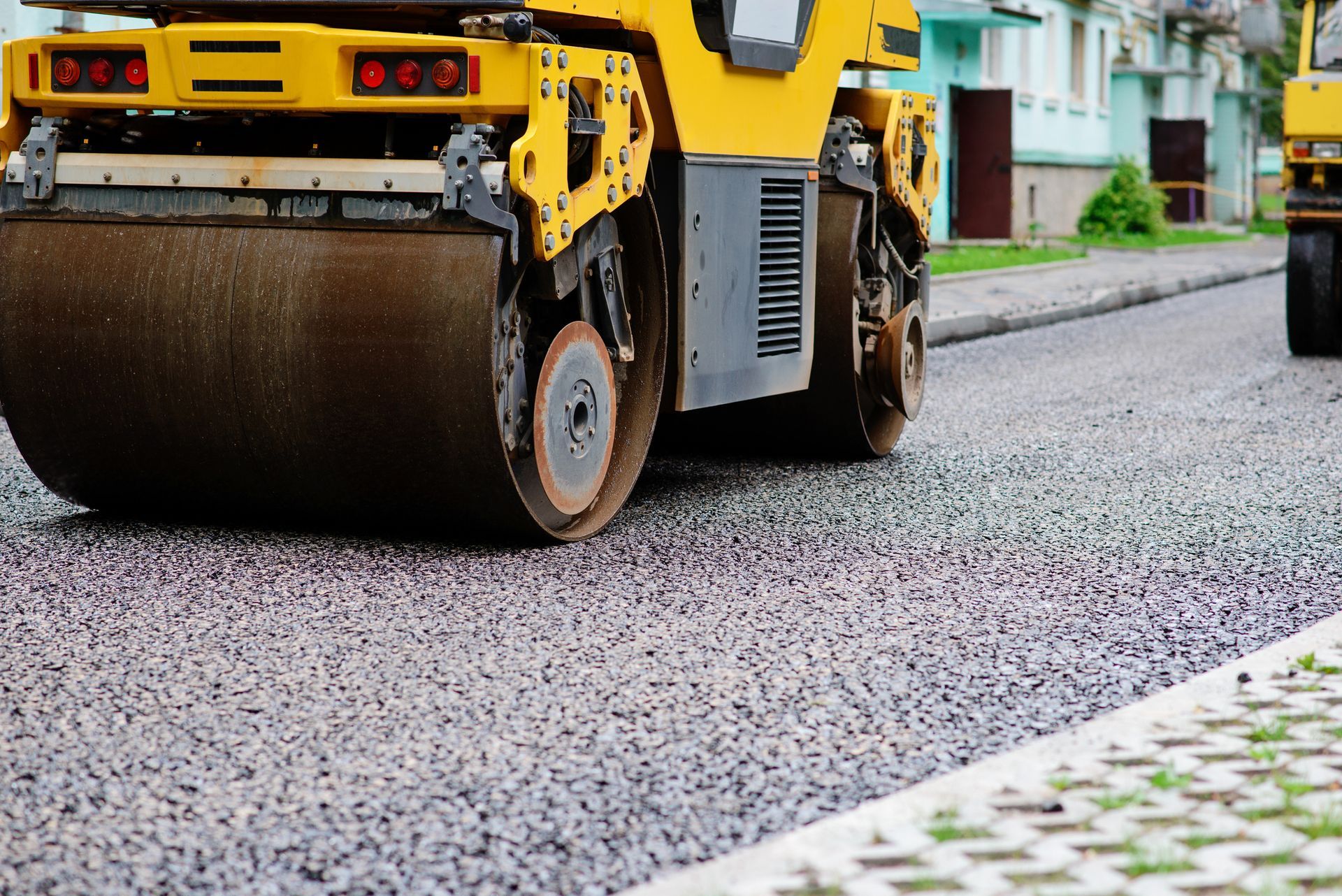 Yellow road roller compacting fresh asphalt during street paving work. Yellow road roller compacting fresh asphalt during street paving work.