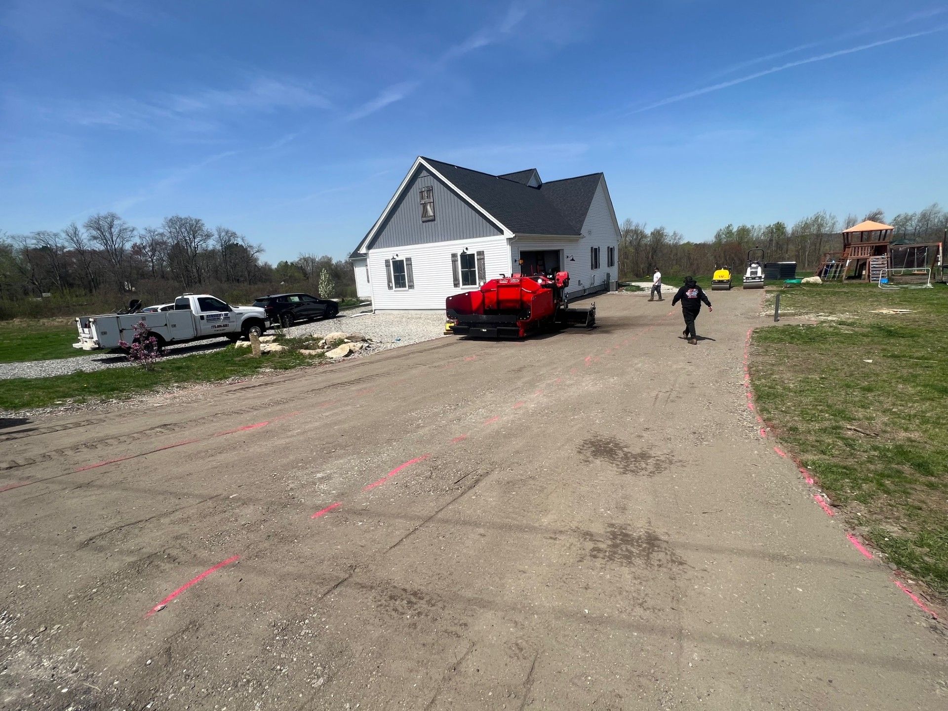 Construction site with a house, gravel driveway, red heavy machinery, and a person walking.