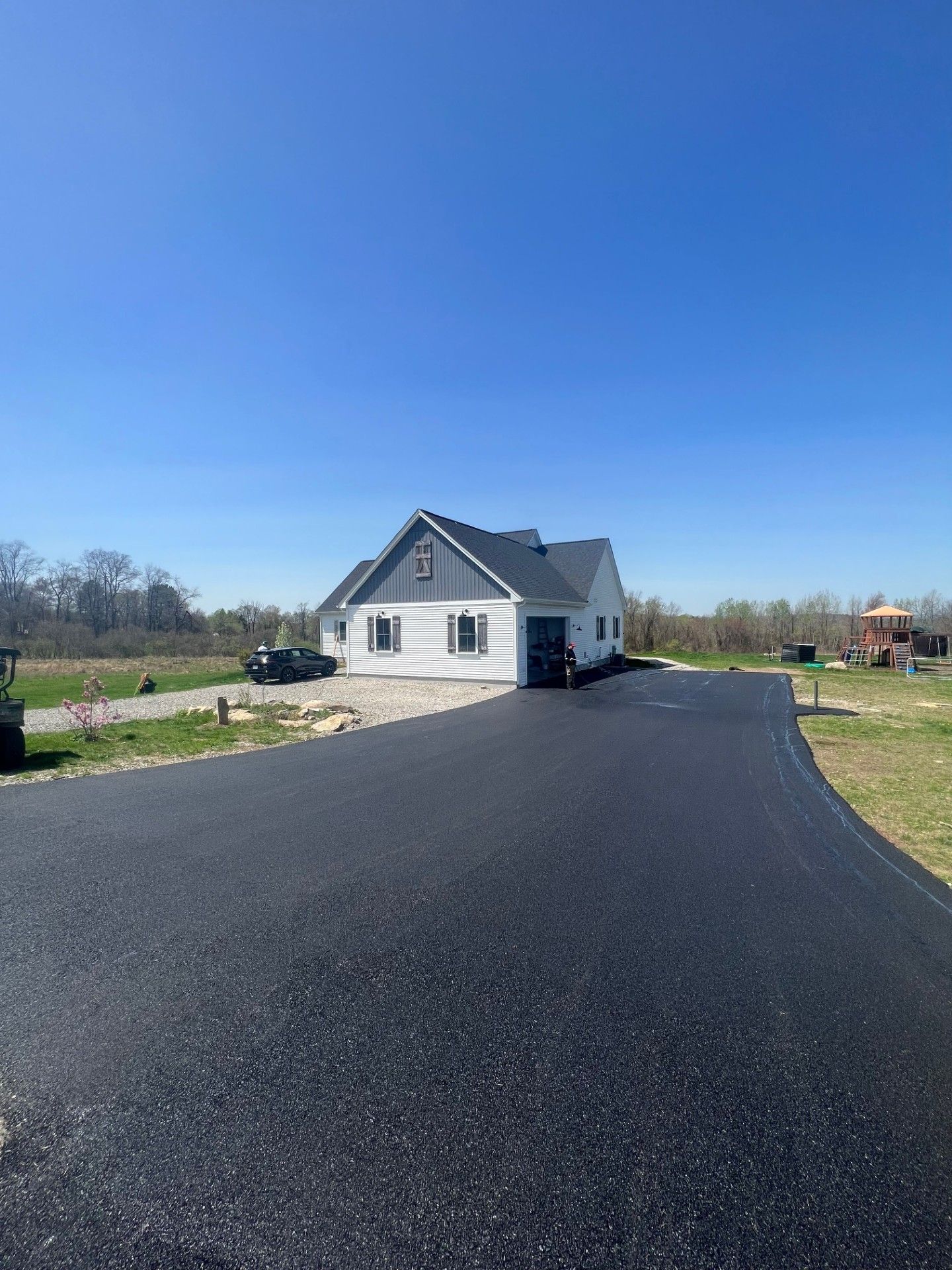 House with a dark paved driveway on a sunny day. White siding with blue and gray accents.