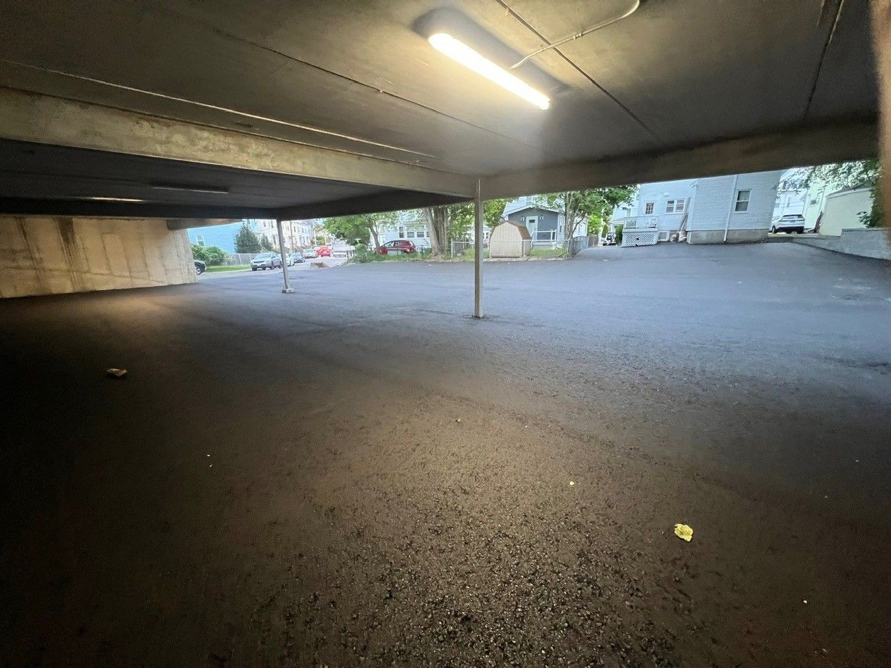View from under a concrete overhang with a paved parking area and buildings in the background.