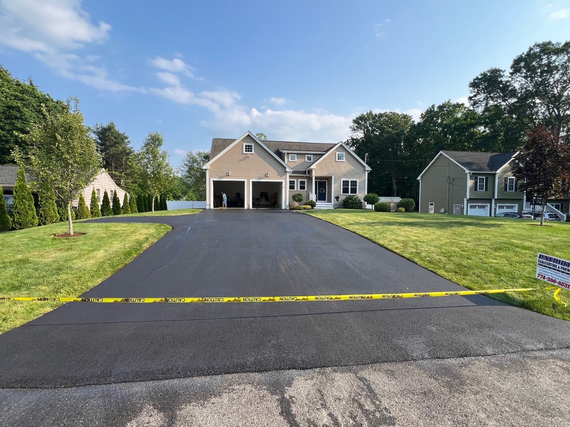 Newly paved asphalt driveway leading to a two-story house with a garage, under a blue sky.