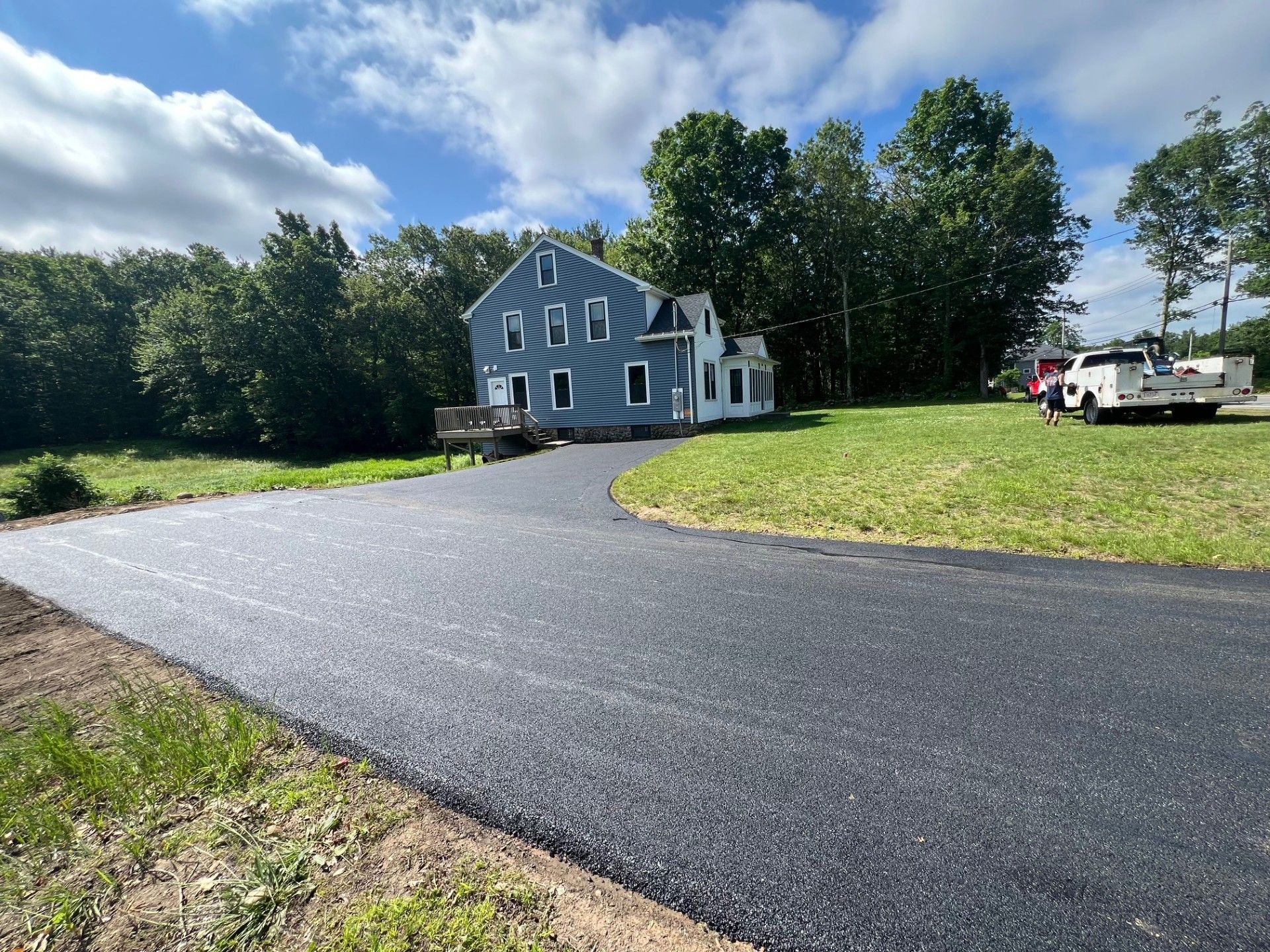 Newly paved black asphalt driveway leading to a blue house on a grassy lot.