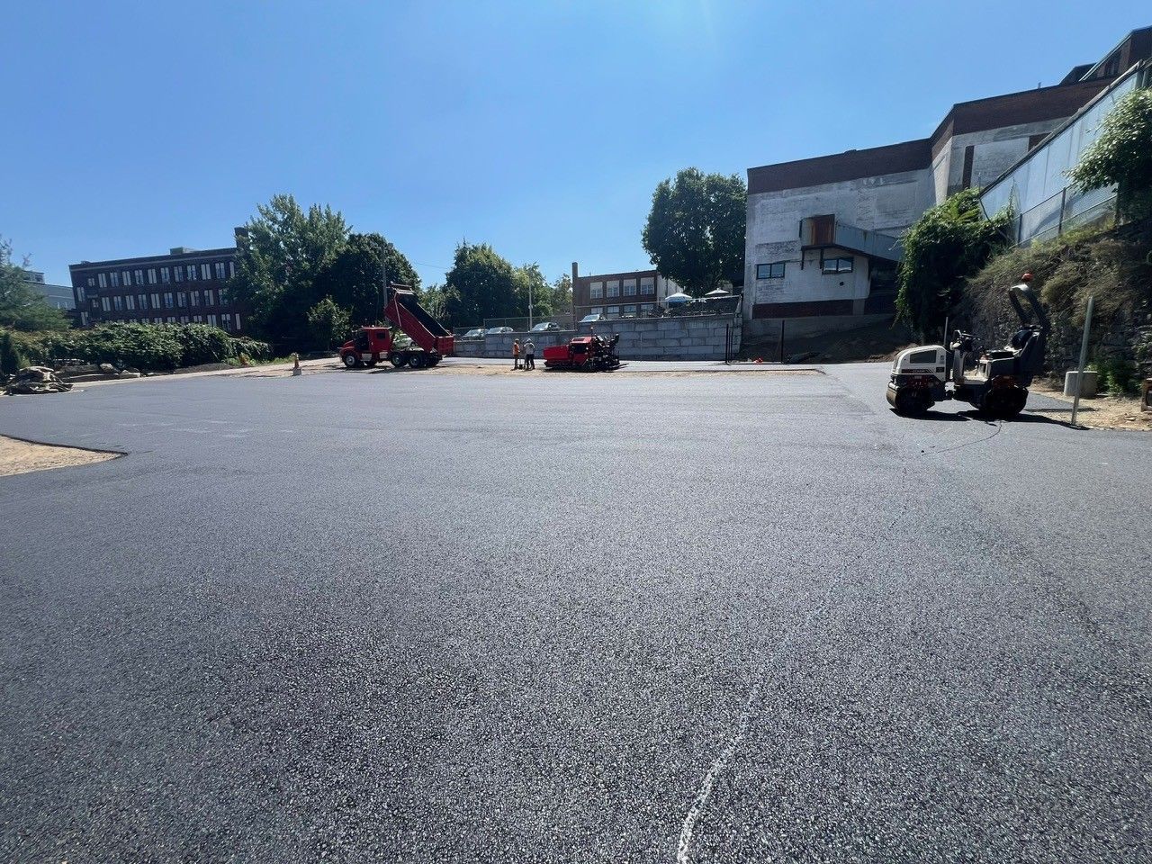 Newly paved asphalt surface with construction equipment in the background under a clear sky.