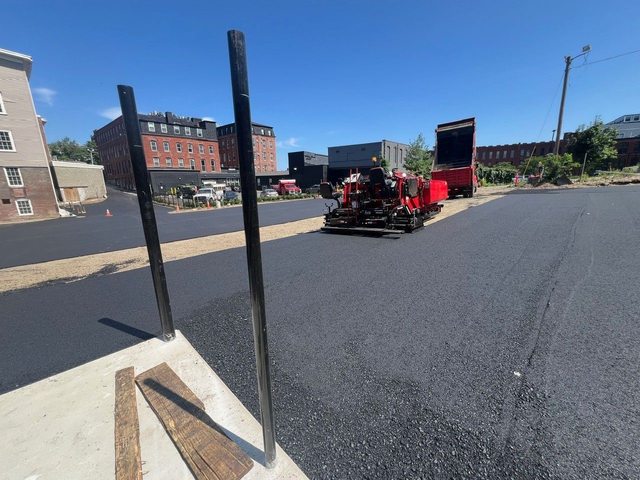 Newly paved asphalt lot with construction equipment; black poles in foreground.