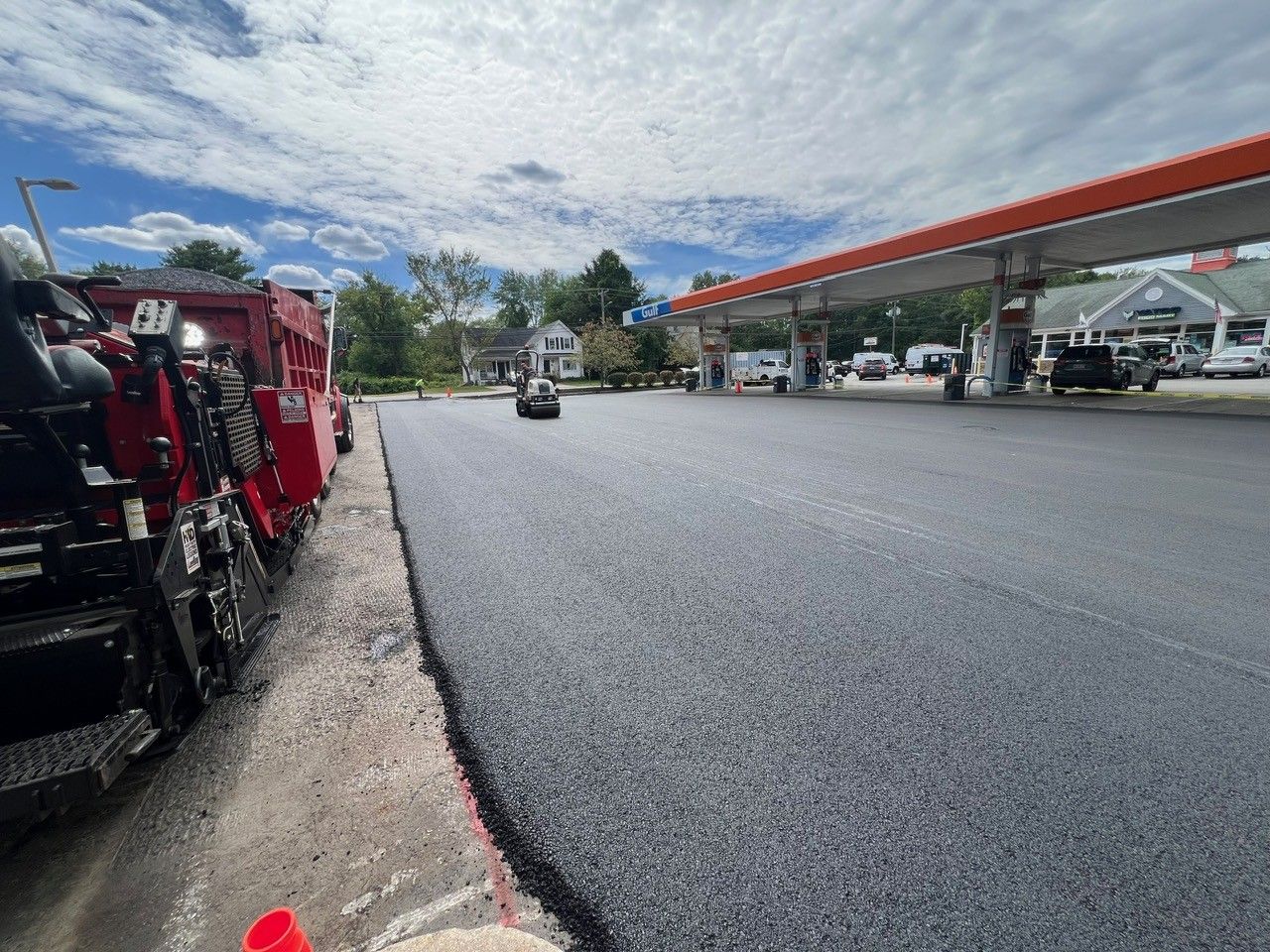 Asphalt paving at a gas station under a blue sky, with the paving machine in view.