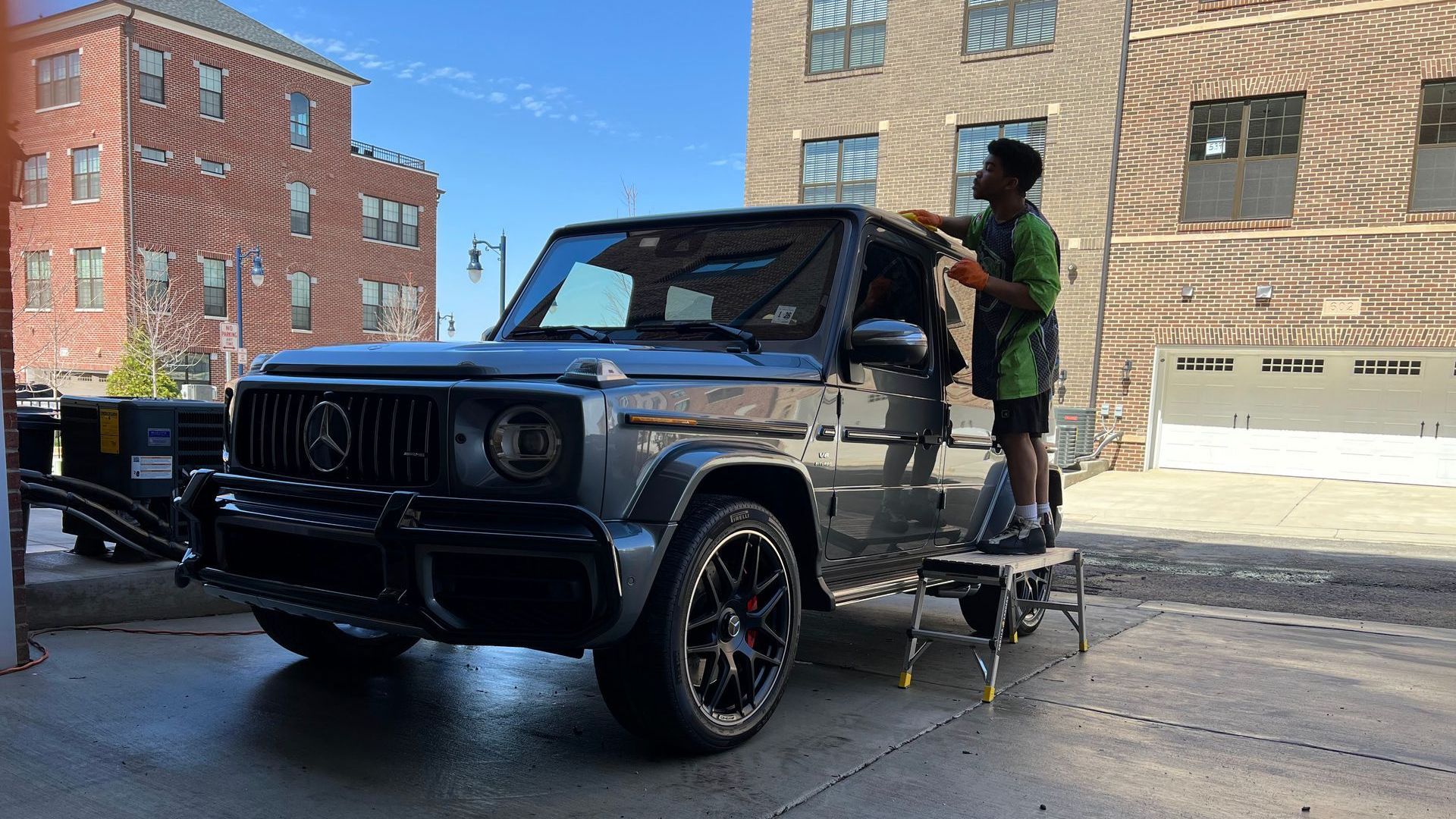 a man is washing a jeep in front of a brick building .