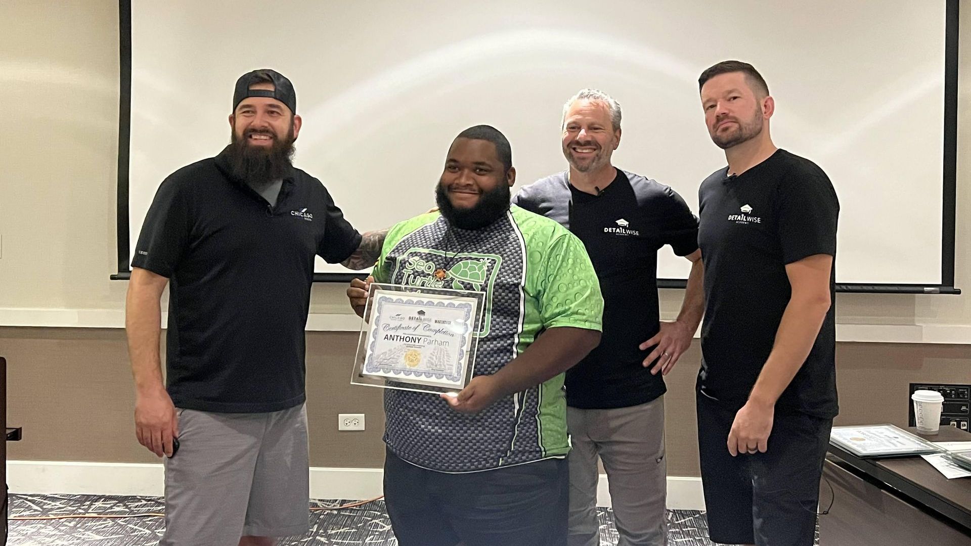 a group of men are standing in front of a projector screen holding a certificate .