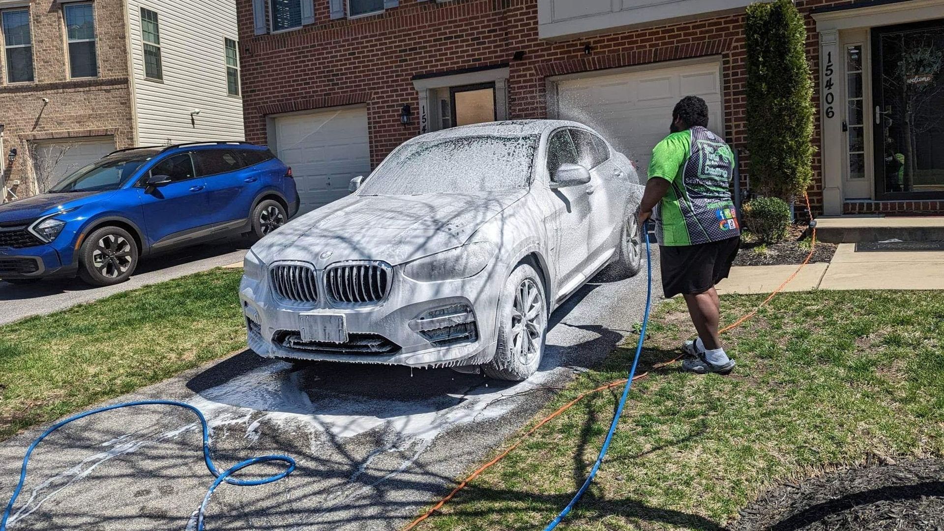 a man is washing a car with foam in front of a house .