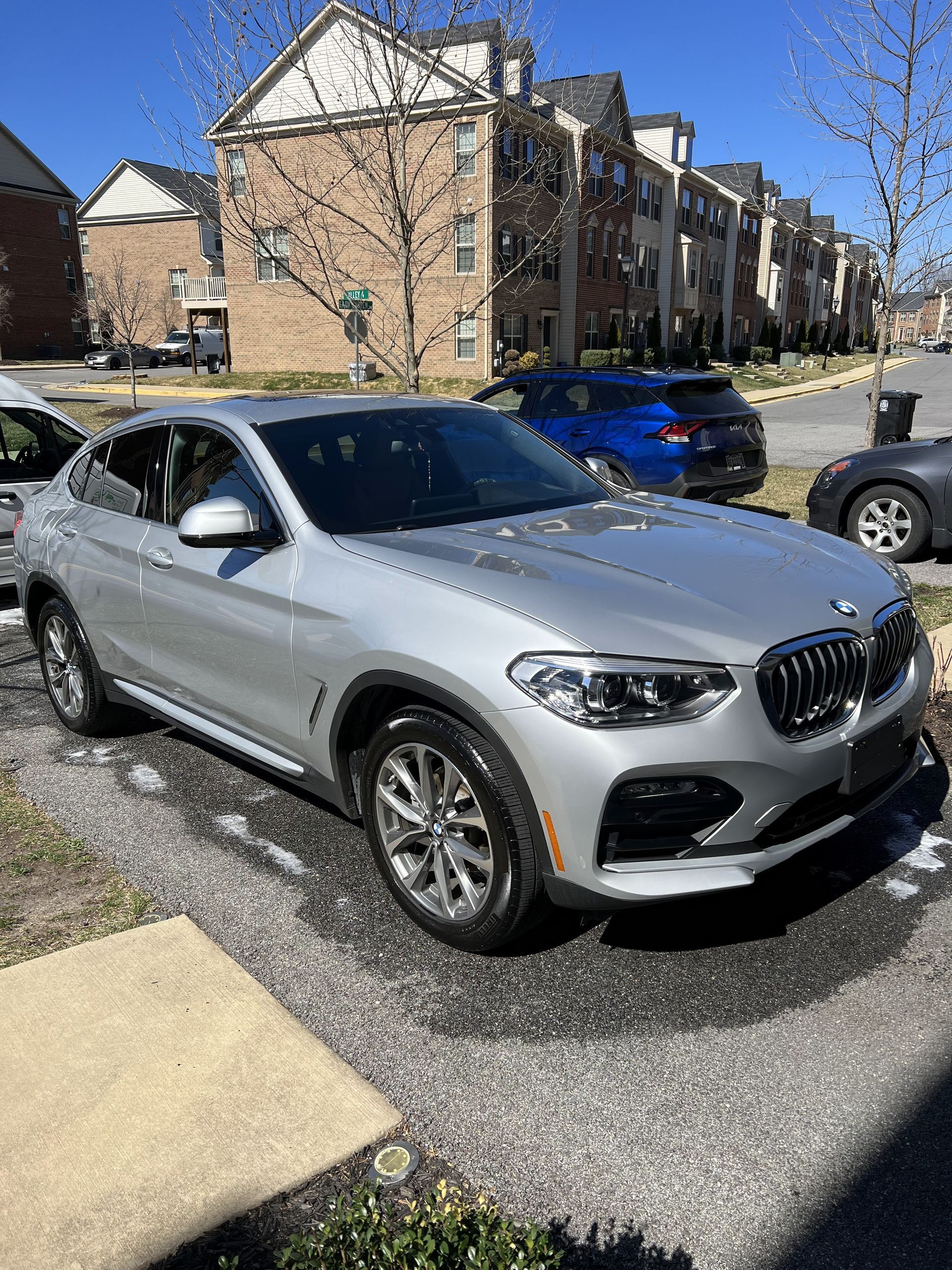 a silver bmw x4 is parked in a parking lot in front of a building .