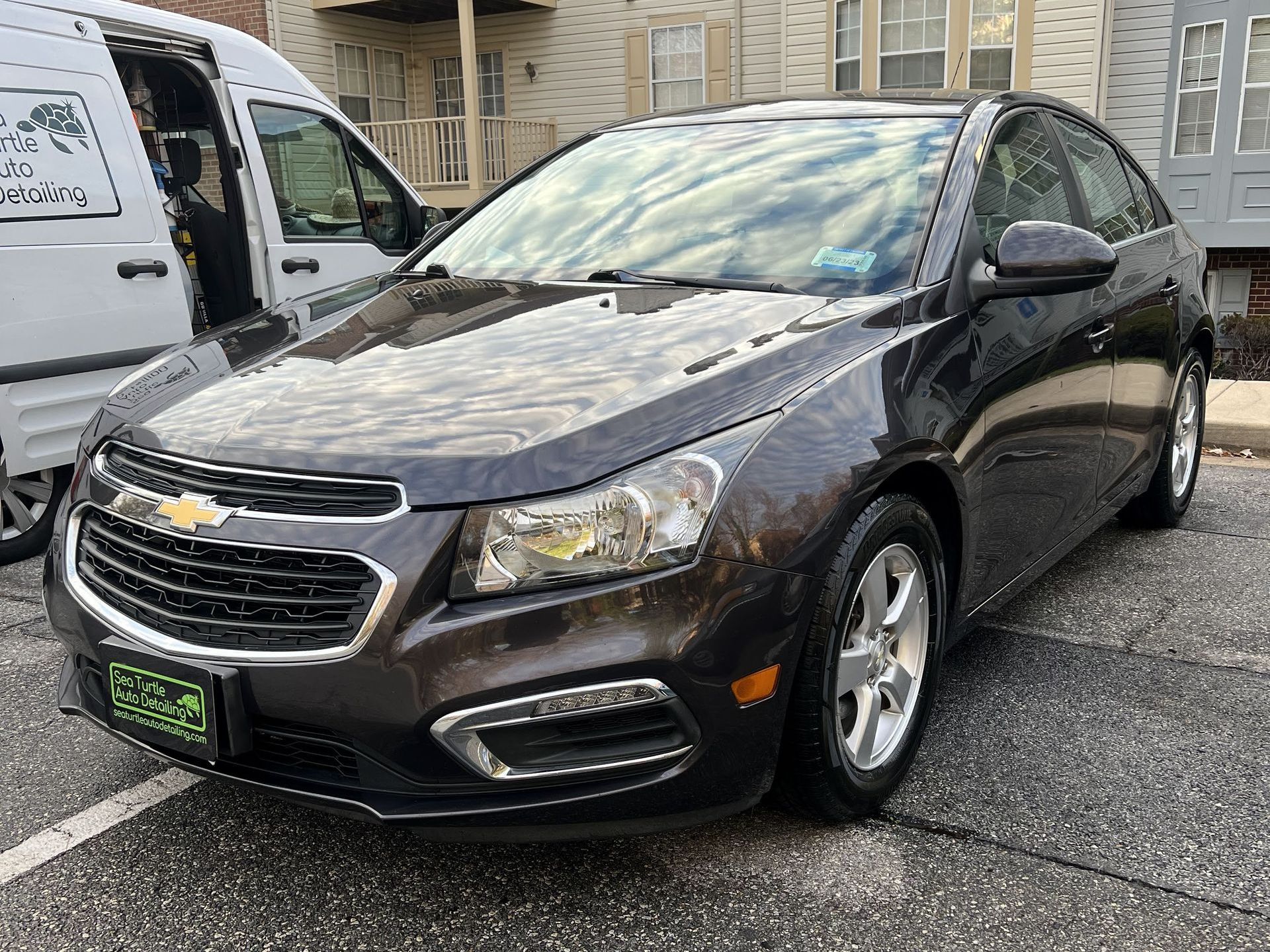 a black chevrolet cruze is parked in a parking lot next to a white van .