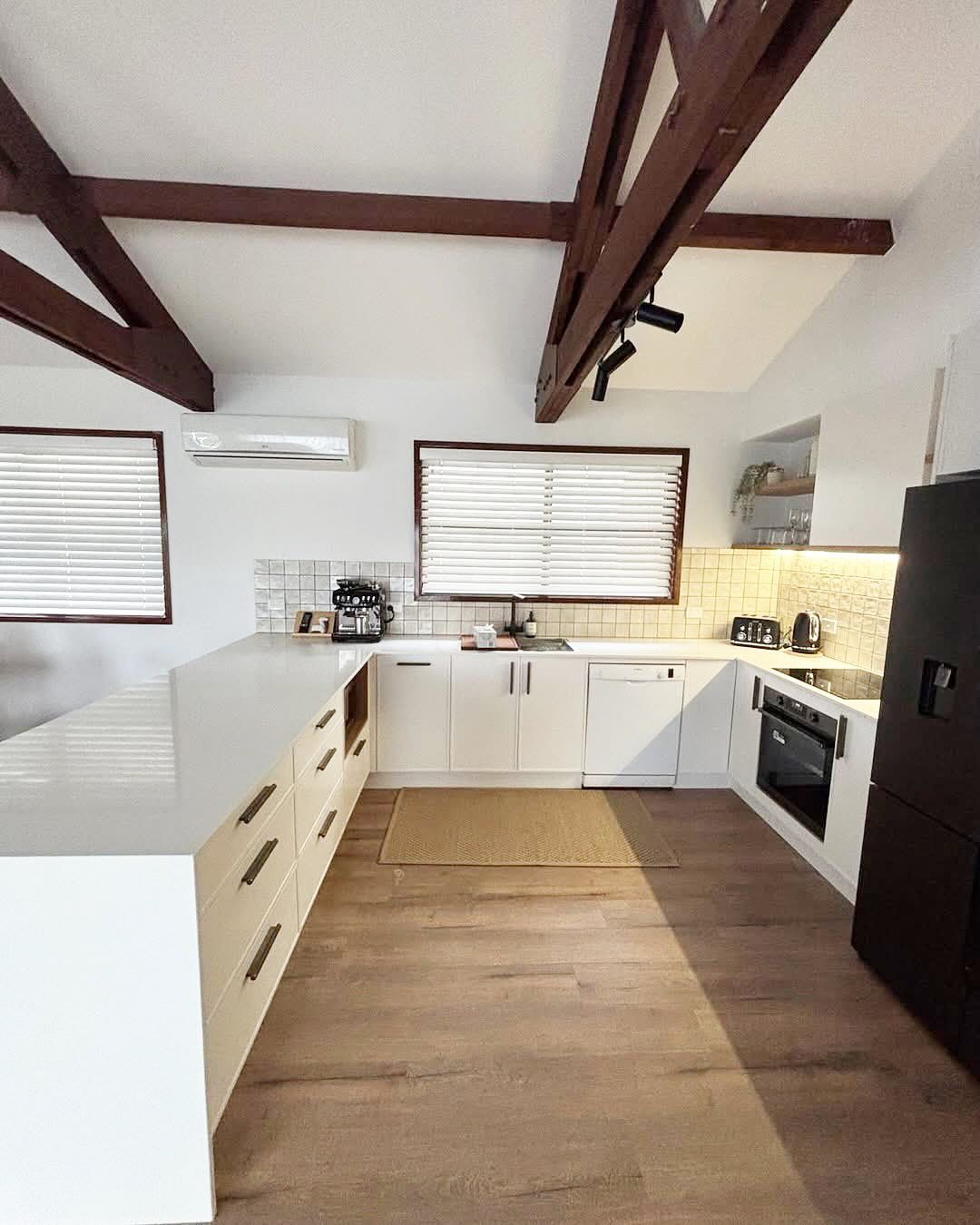 White kitchen with wood beams, white cabinets, and a black refrigerator — CPAINT In Kempsey, NSW