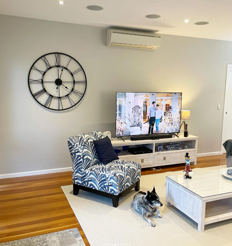 Living room with a large clock, armchair, TV, dog, and a white coffee table. — CPAINT in Forster, NSW
