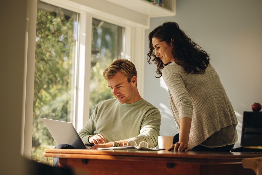 a man and a woman are looking at a laptop computer .