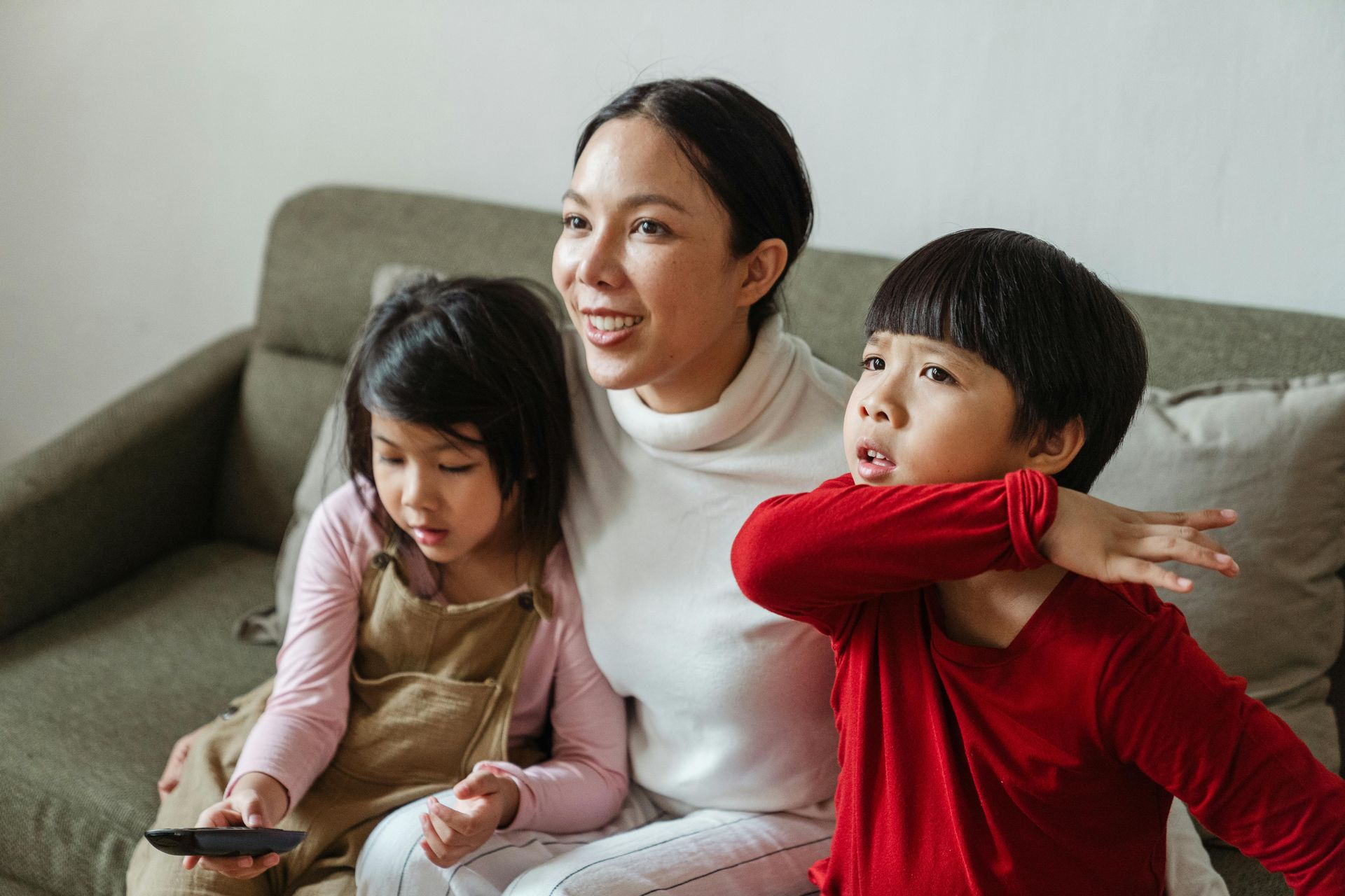 Woman and two children watch TV on a couch. One child covers their mouth.