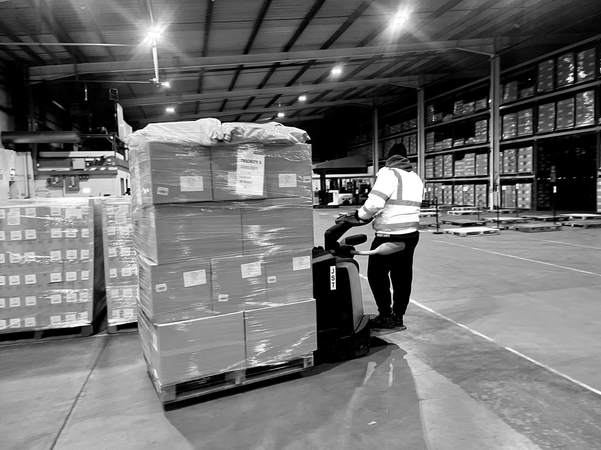 A black and white photo of a large NSK Fulfilment warehouse filled with lots of boxes.