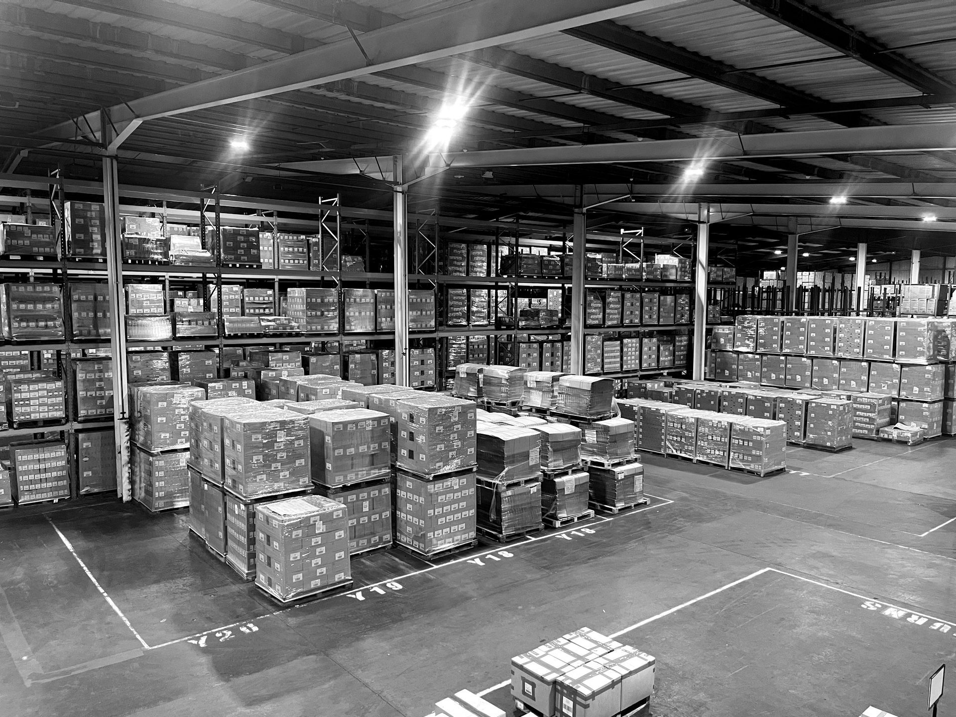 A black and white photo of a large NSK Fulfilment warehouse filled with lots of boxes.