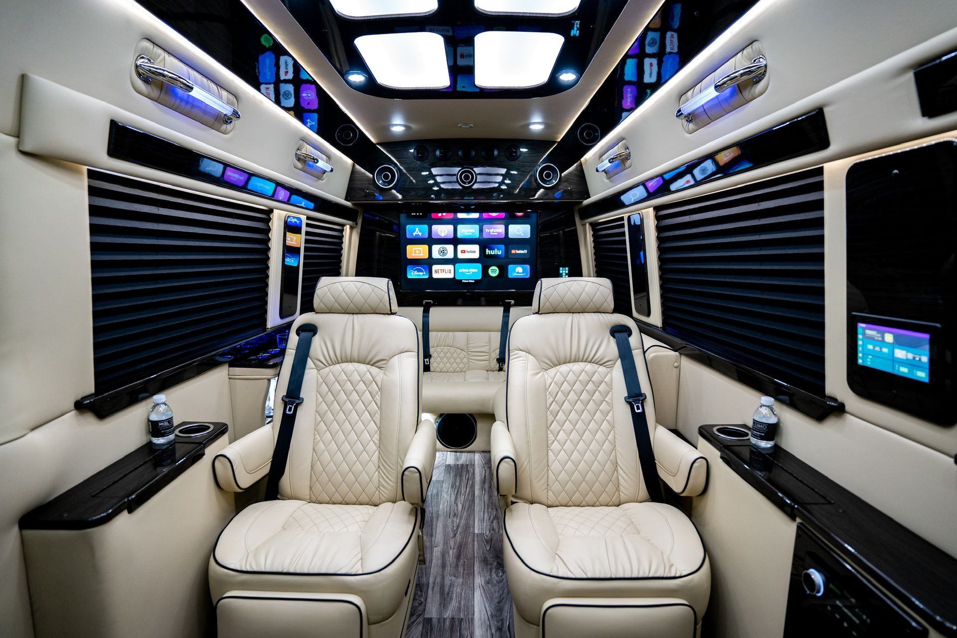 Luxurious van interior with cream leather seats, multiple screens, and black window shades.