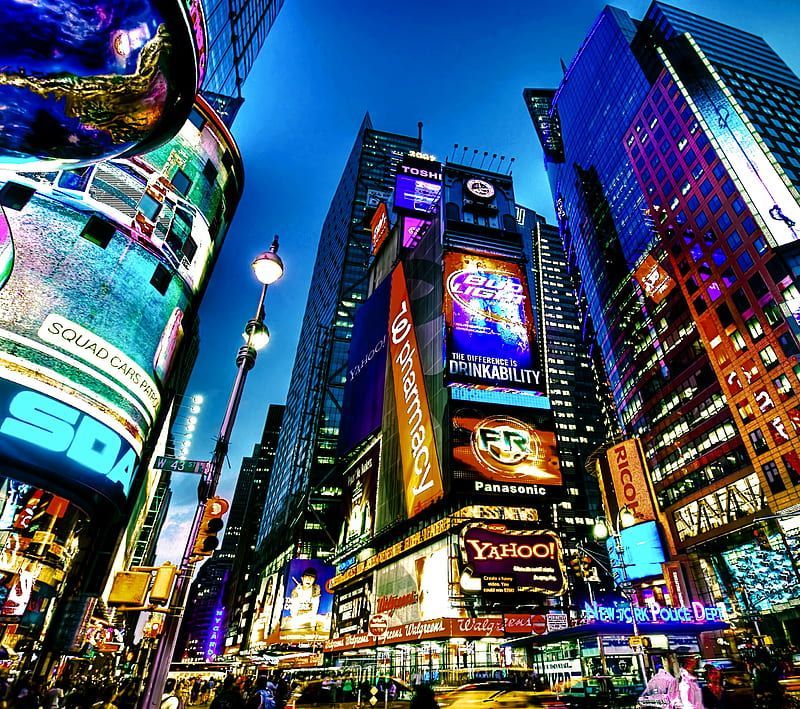 Times Square at dusk, illuminated by colorful billboards and streetlights, with tall buildings.