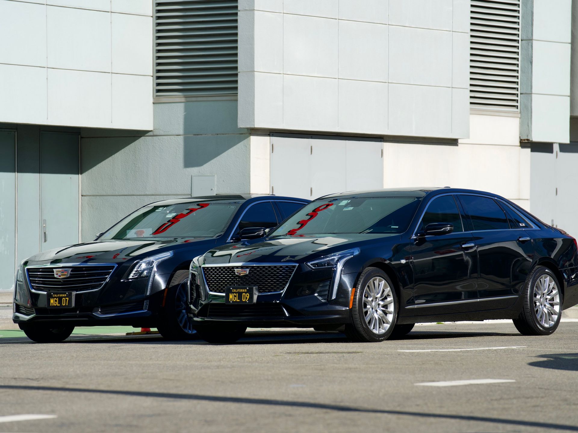 Two black Cadillac sedans parked on a city street in front of a modern building.