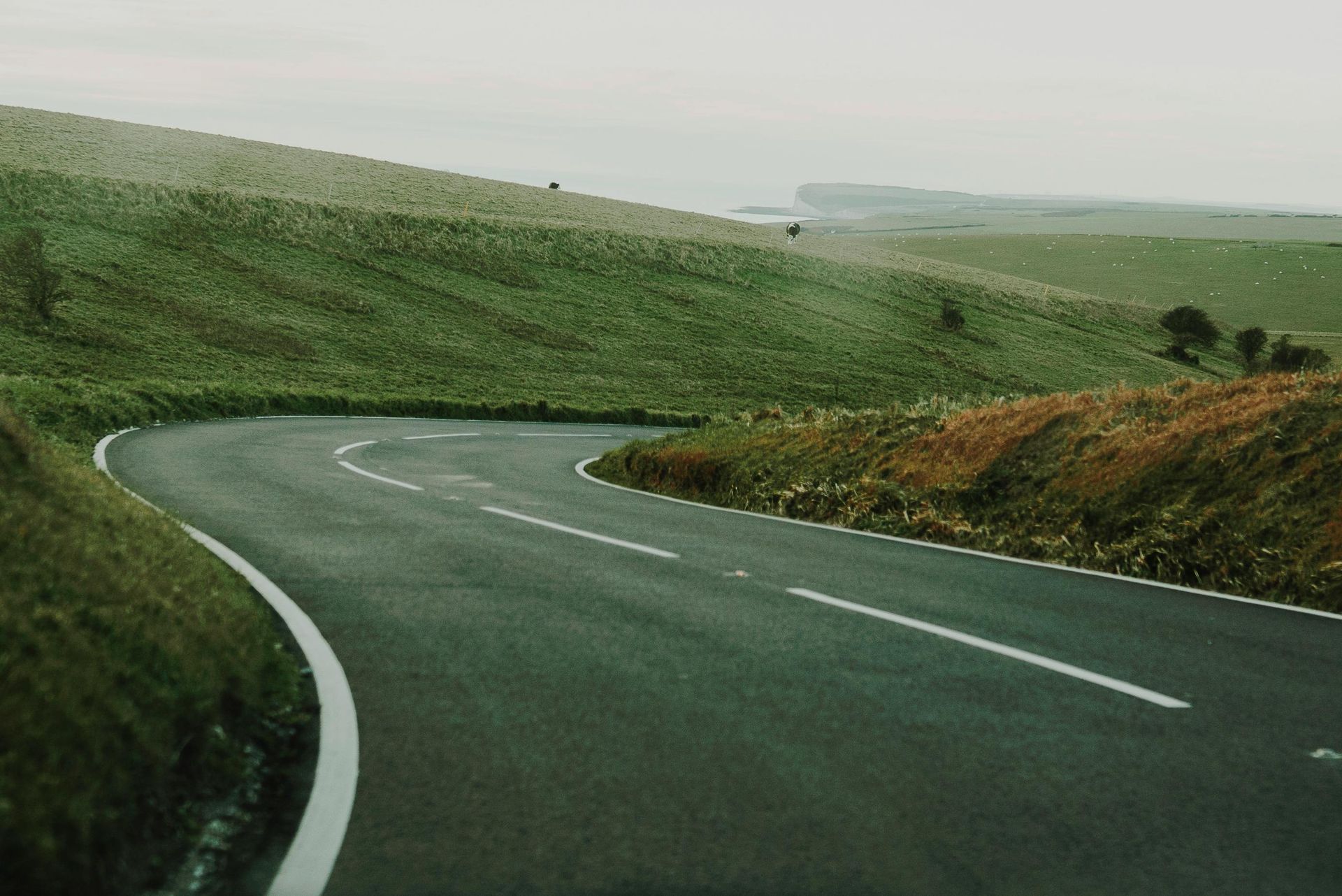 Curving asphalt road winds through green hills under an overcast sky.