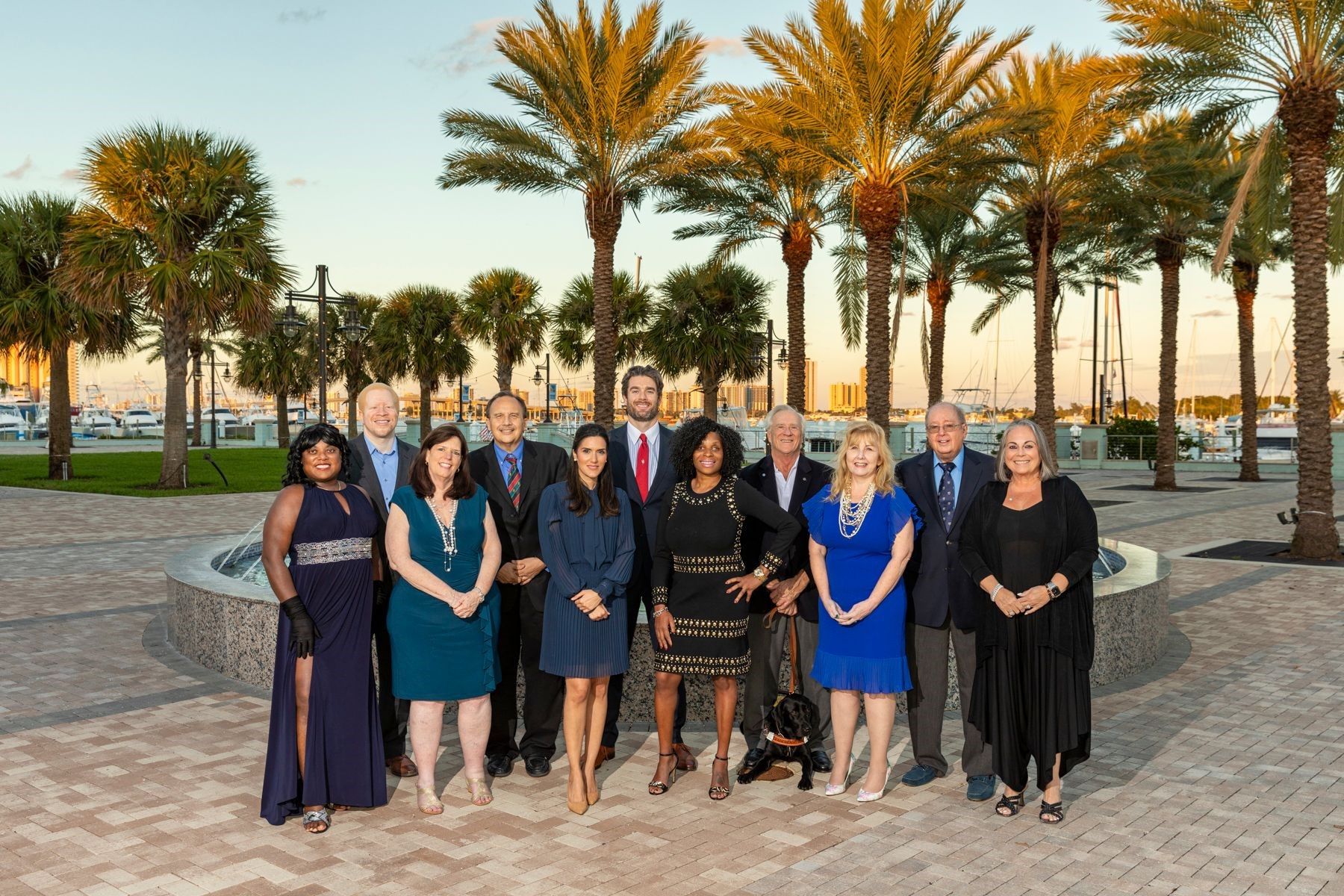 Lighthouse for the Blind of the Palm Beaches Board Members pose in front of a beach scene with boats and palm trees in the background.