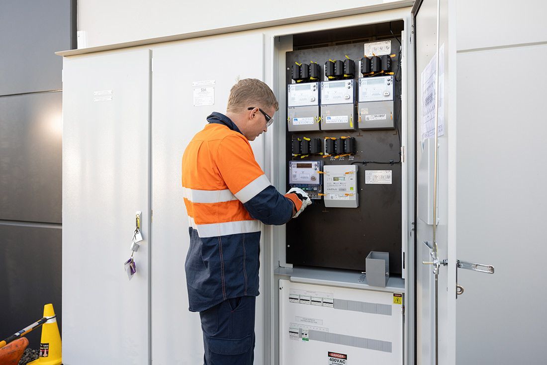 A Man in an Orange and Blue Safety Vest is Working on an Electrical Box — Macquarie Electric in Brisbane, QLD