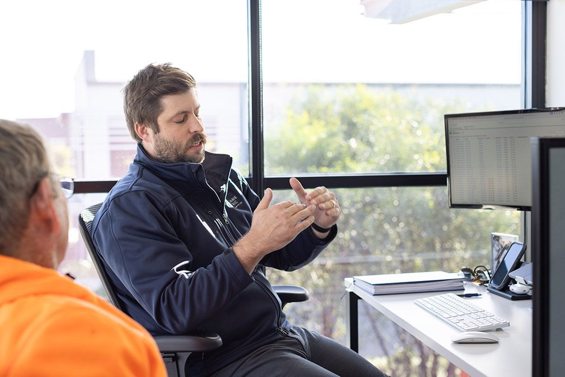 A Man is Sitting at a Desk Talking to Another Man — Macquarie Electric in Dubbo, NSW