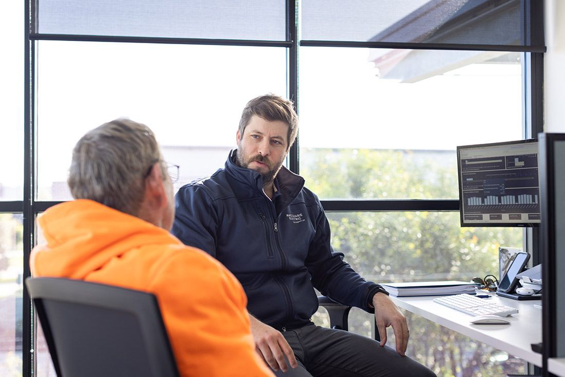 Two Men Are Sitting at a Desk Talking to Each Other — Macquarie Electric in Dubbo, NSW