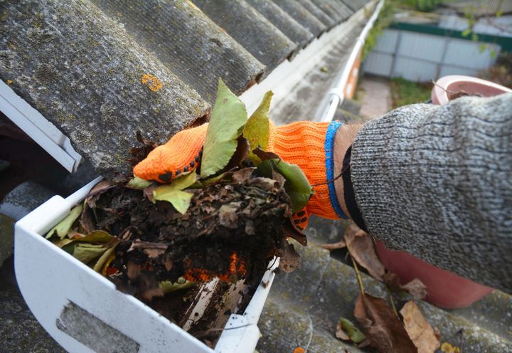 A person wearing orange gloves is cleaning a gutter on a roof.