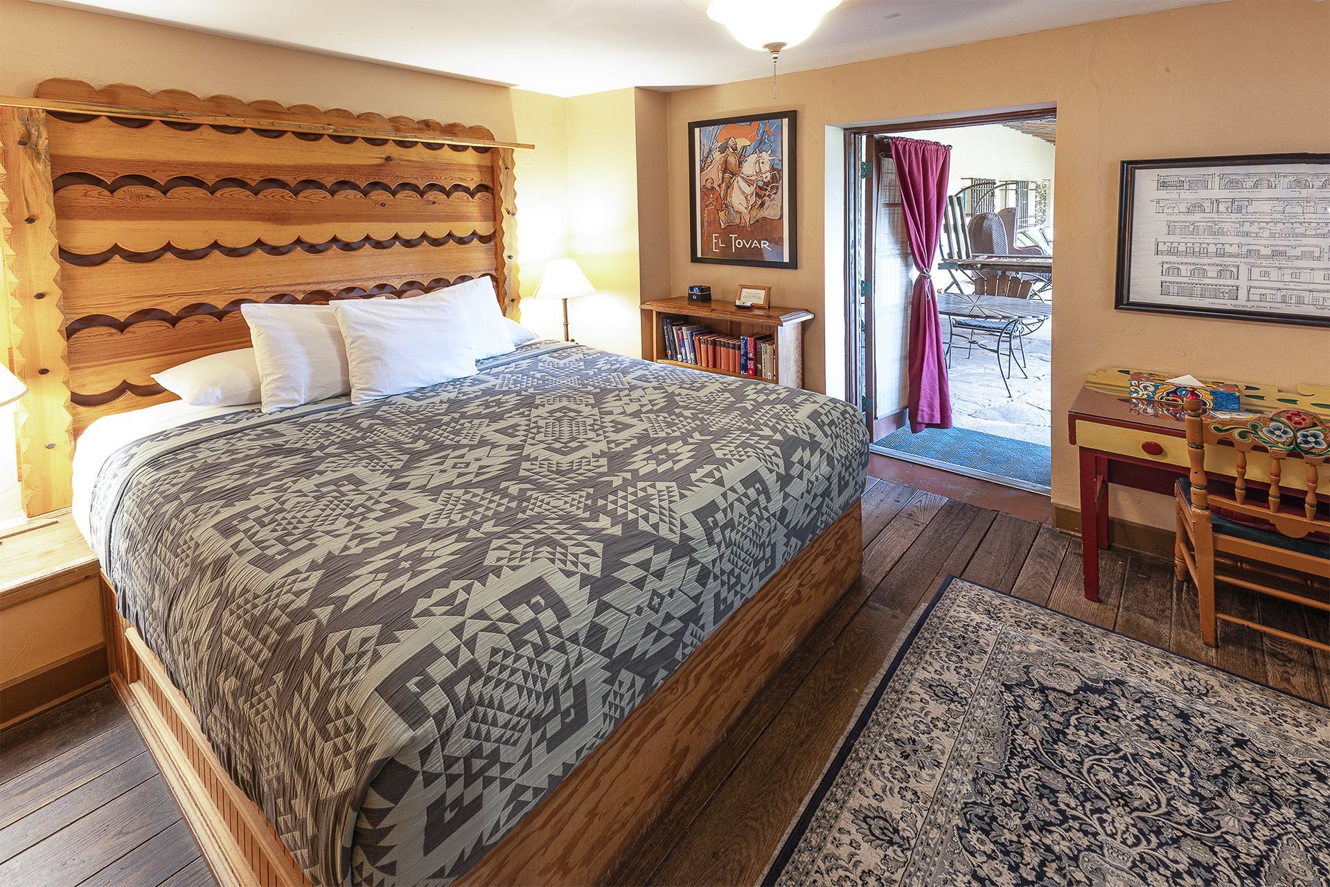 Bedroom with wooden bed frame, patterned quilt, desk, and door to a balcony.